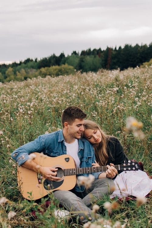 A Man Playing an Acoustic Guitar and Woman Laying her Head on his Shoulder 