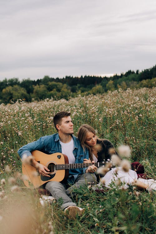 A Male Playing an Acoustic Guitar and Female Laying Her Head on His Shoulder 