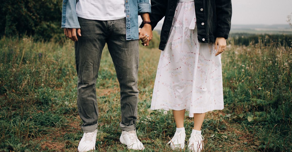 A couple holds hands in a green field, showcasing casual fashion and romantic connection.