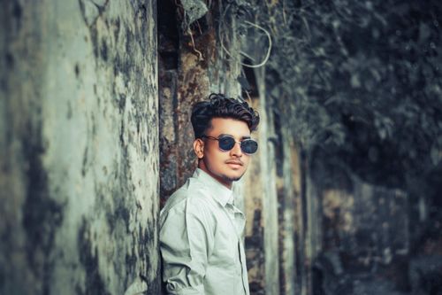 Free Young man in sunglasses leaning against a textured concrete wall outdoors. Stock Photo