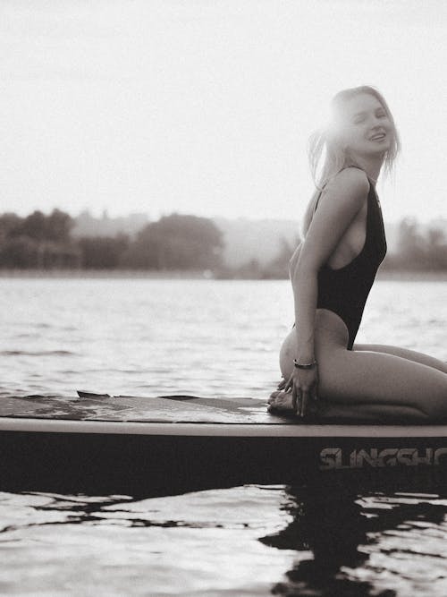 Free Beautiful Young Woman Kneeling on Surfboard Floating on Lake Stock Photo