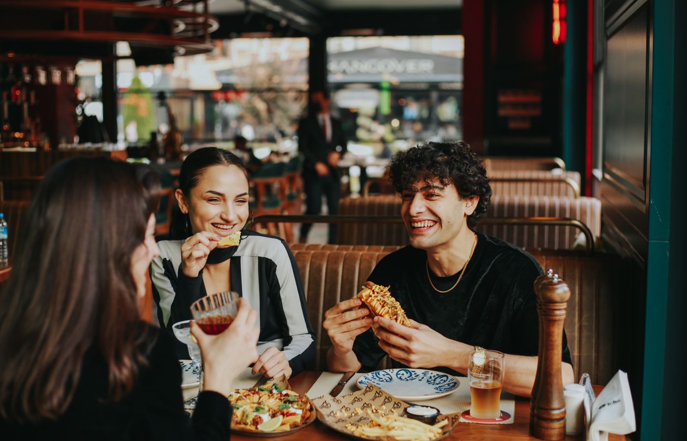 Group of friends laughing and eating at a restaurant, enjoying leisure time.