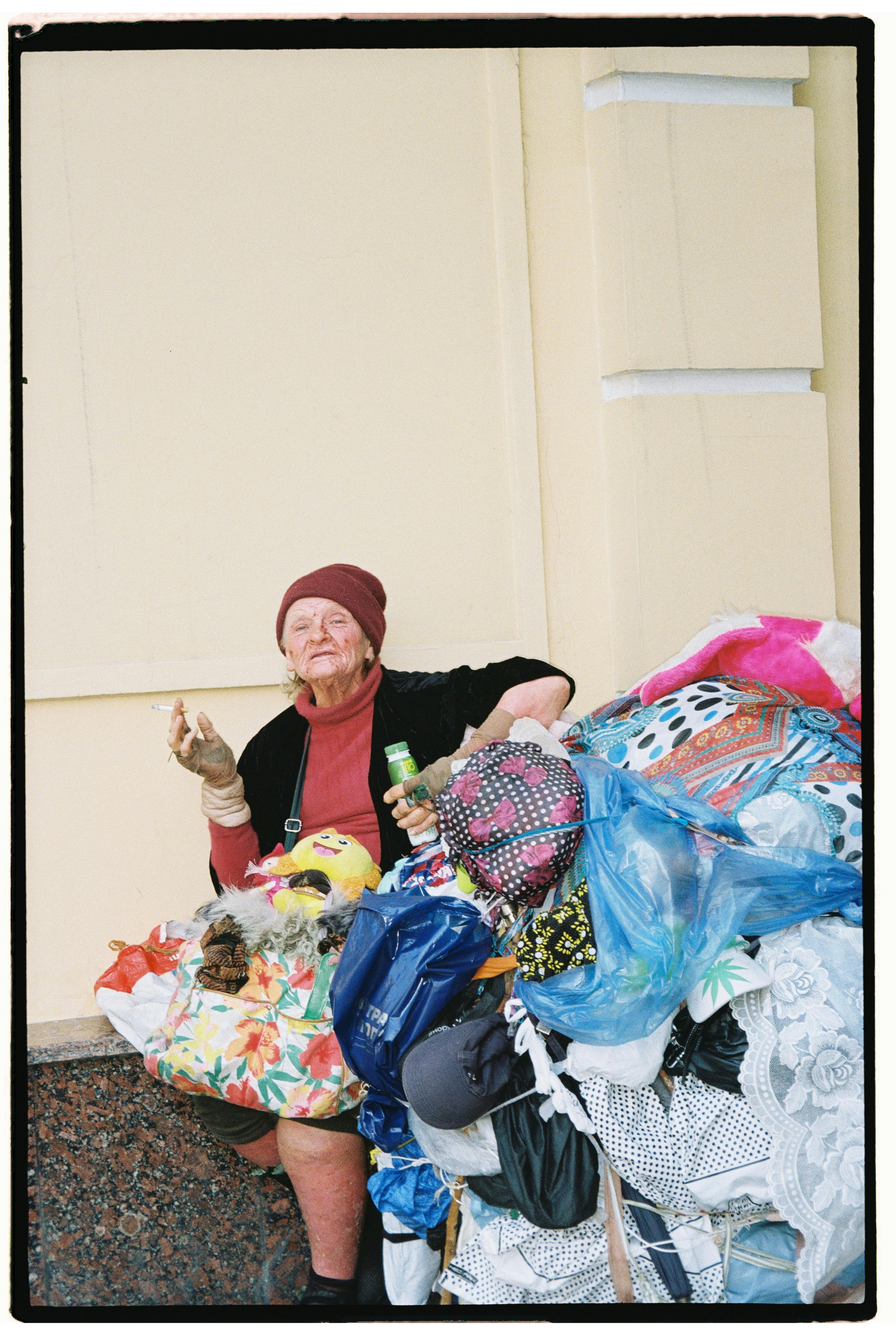 Senior adult woman sitting with a collection of colorful bags outdoors, smoking.