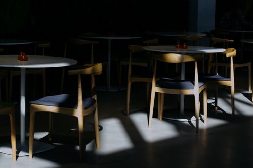 Free A dimly lit indoor cafe features sunlight casting shadows on modern chairs and tables. Stock Photo