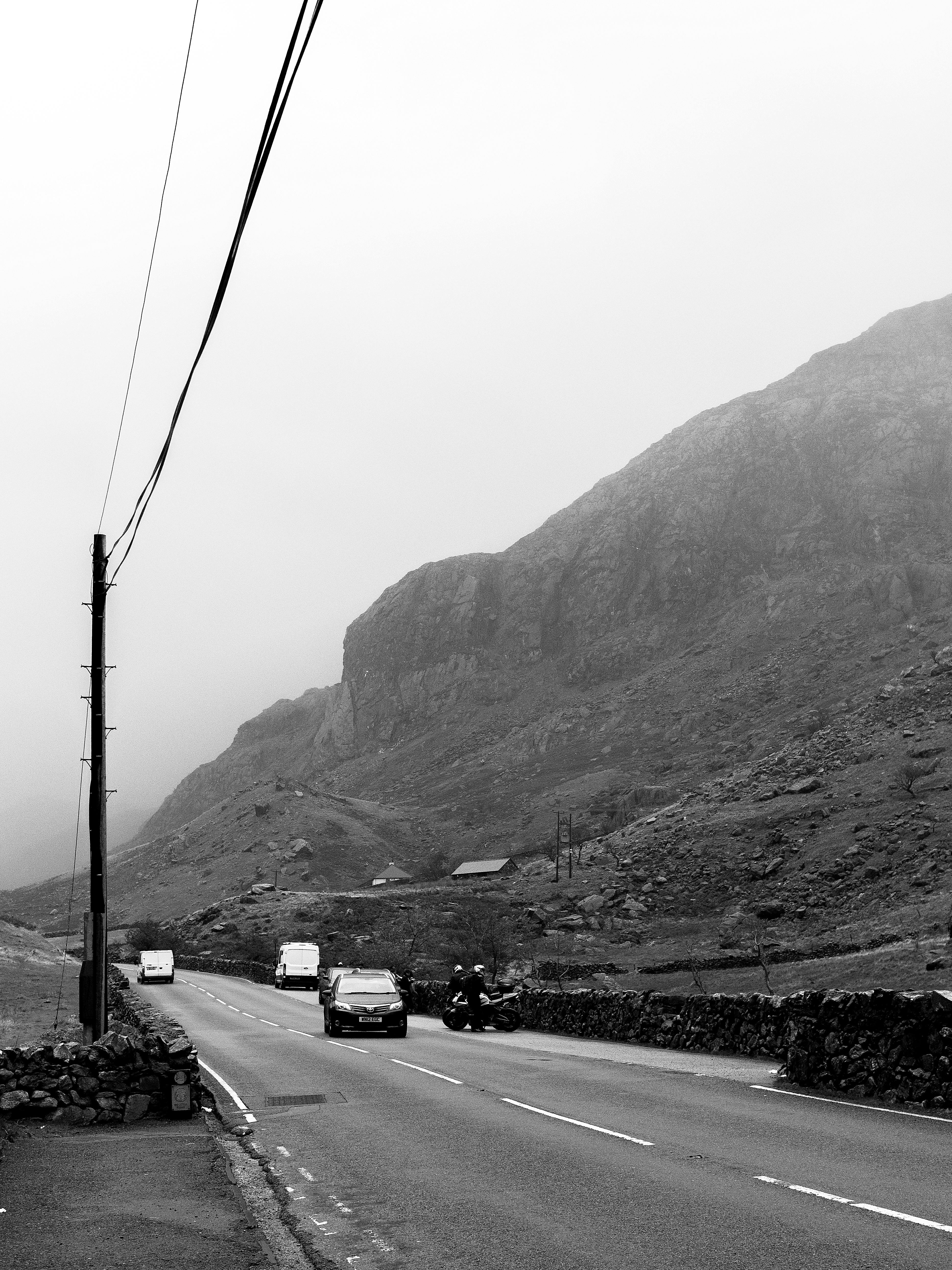 Black and white photo of a foggy mountain road with cars driving in Wales, United Kingdom.