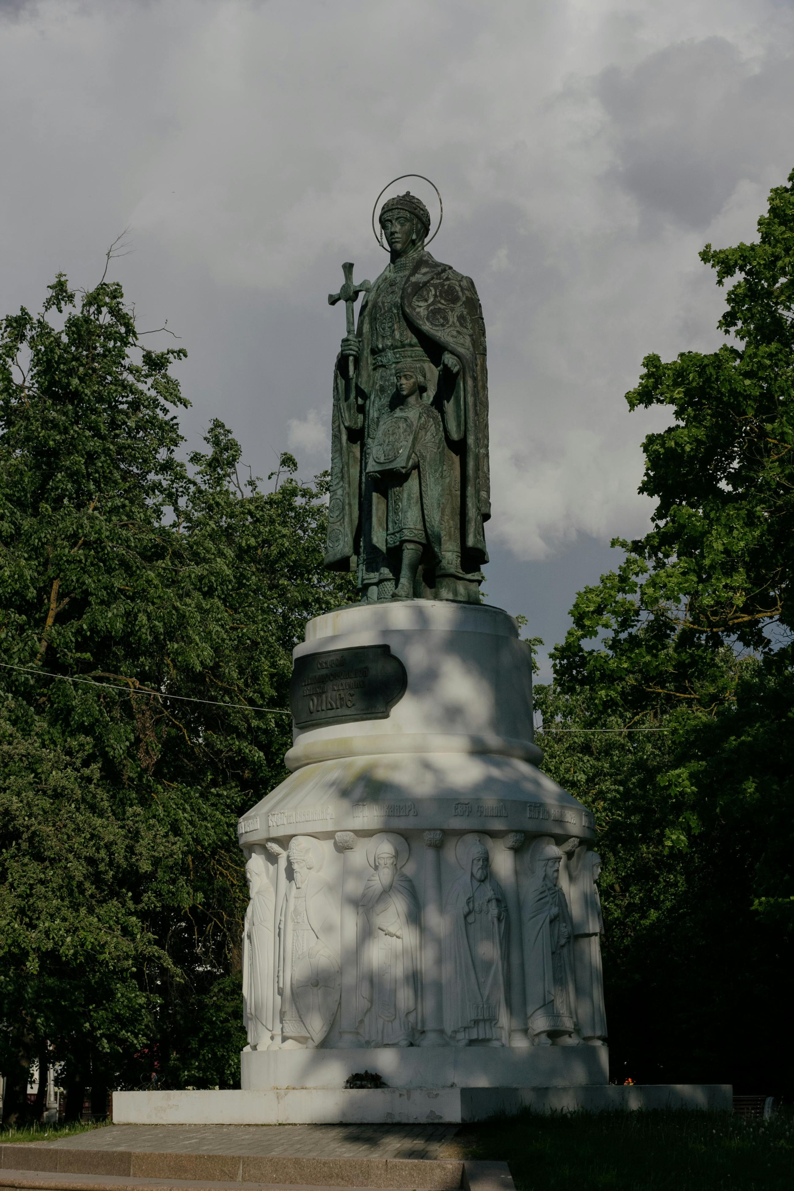 Statue of a religious figure on a pedestal surrounded by trees, emphasizing spirituality and history.