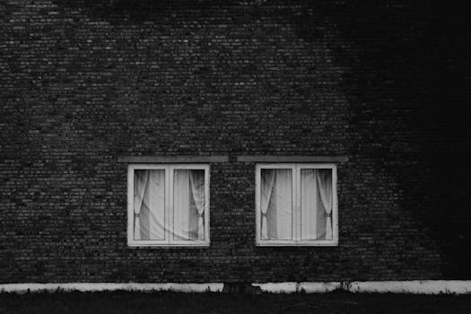 Monochrome photo of a brick wall featuring two curtained windows.