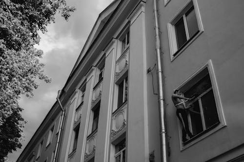 Grayscale Photo of Man Cleaning a Window of a Concrete Building