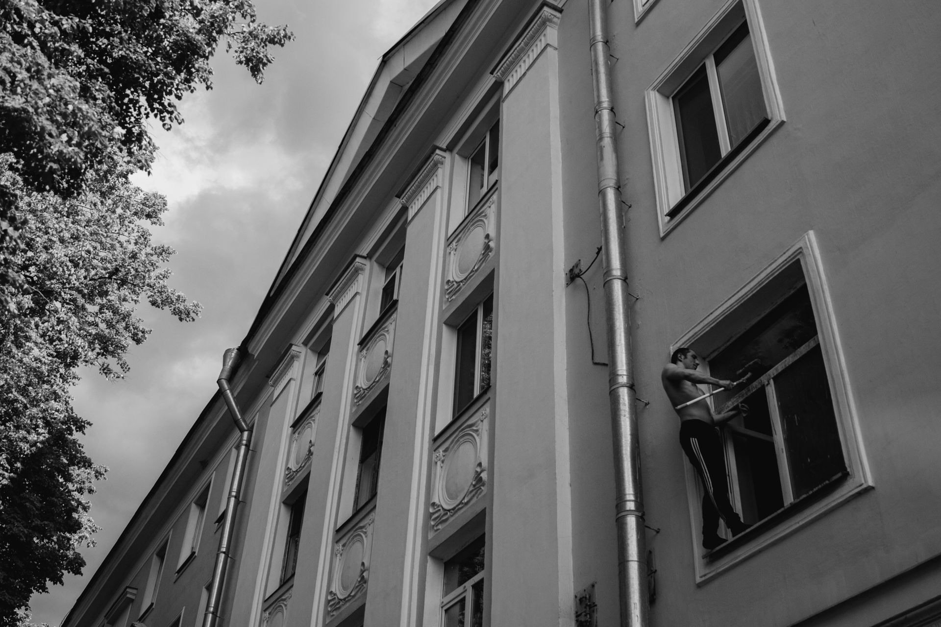Grayscale Photo of Man Cleaning a Window of a Concrete Building