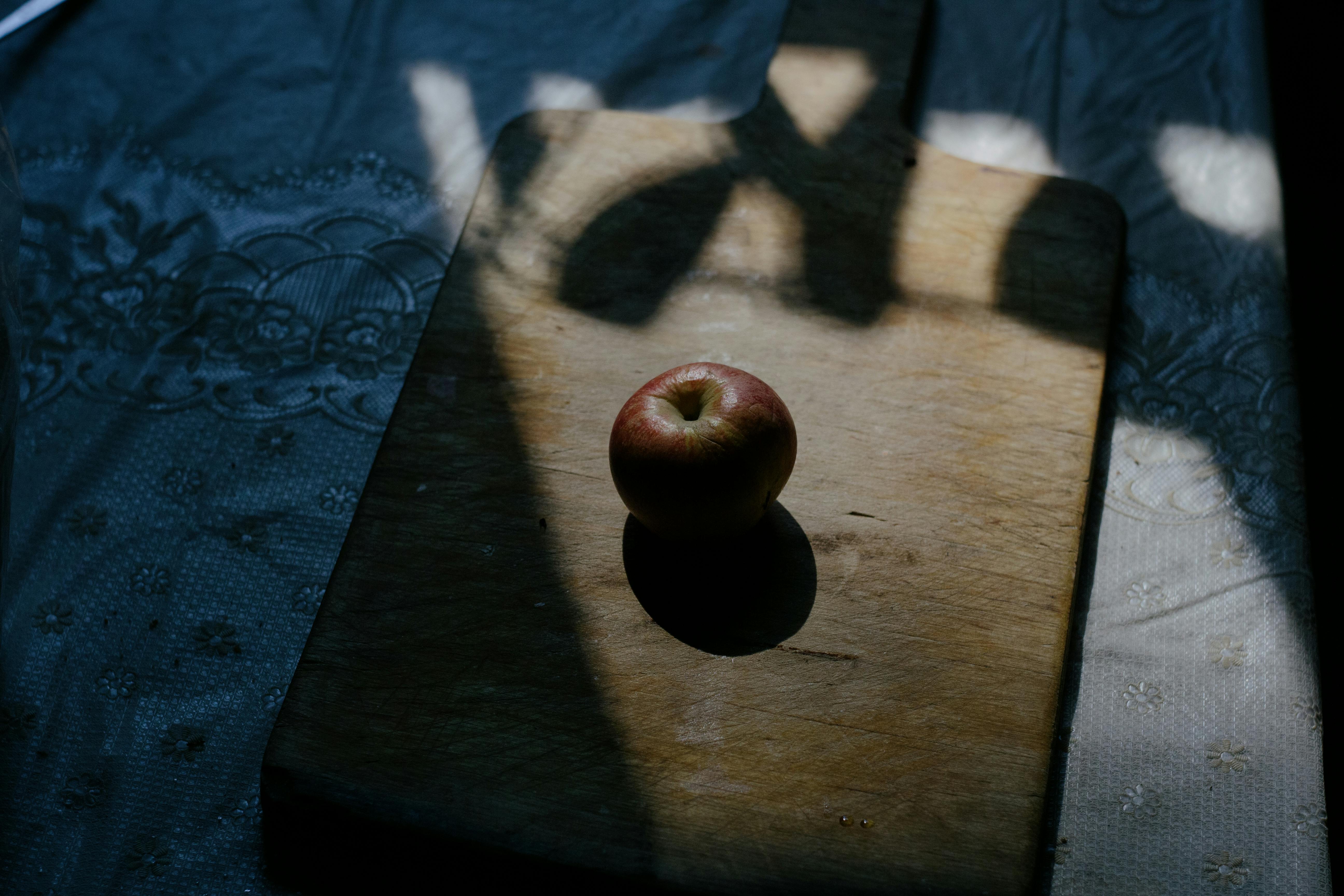 Sunlit apple on a wooden cutting board with dramatic shadows.