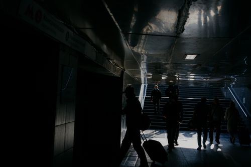 Free Silhouetted figures walking through a dimly lit subway tunnel with stairs leading to the surface. Stock Photo
