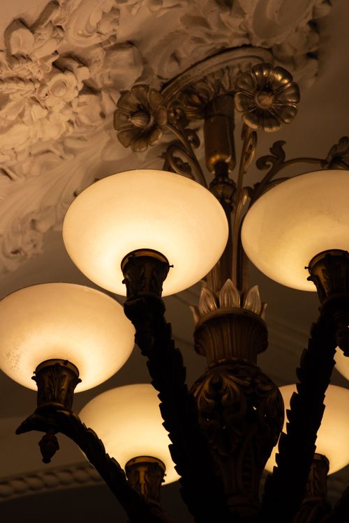 Free Close-up of a decorative chandelier illuminating an ornate ceiling in a luxurious setting. Stock Photo