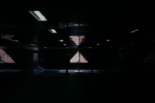 Free A dark, reflective interior space with a silhouette of a person standing amidst the light and shadows. Stock Photo