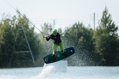 Free Action shot of a man wakeboarding and performing a high jump in an outdoor setting. Stock Photo