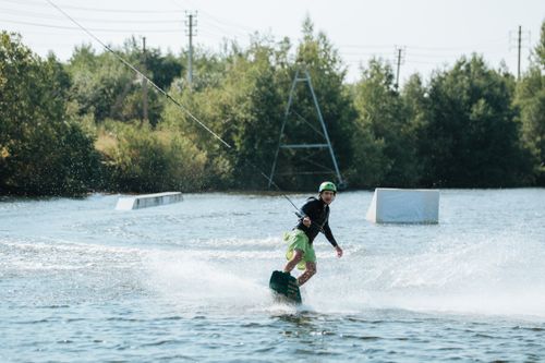 Free An adventurous man wakeboarding on a tranquil lake, creating a dynamic and thrilling scene. Stock Photo