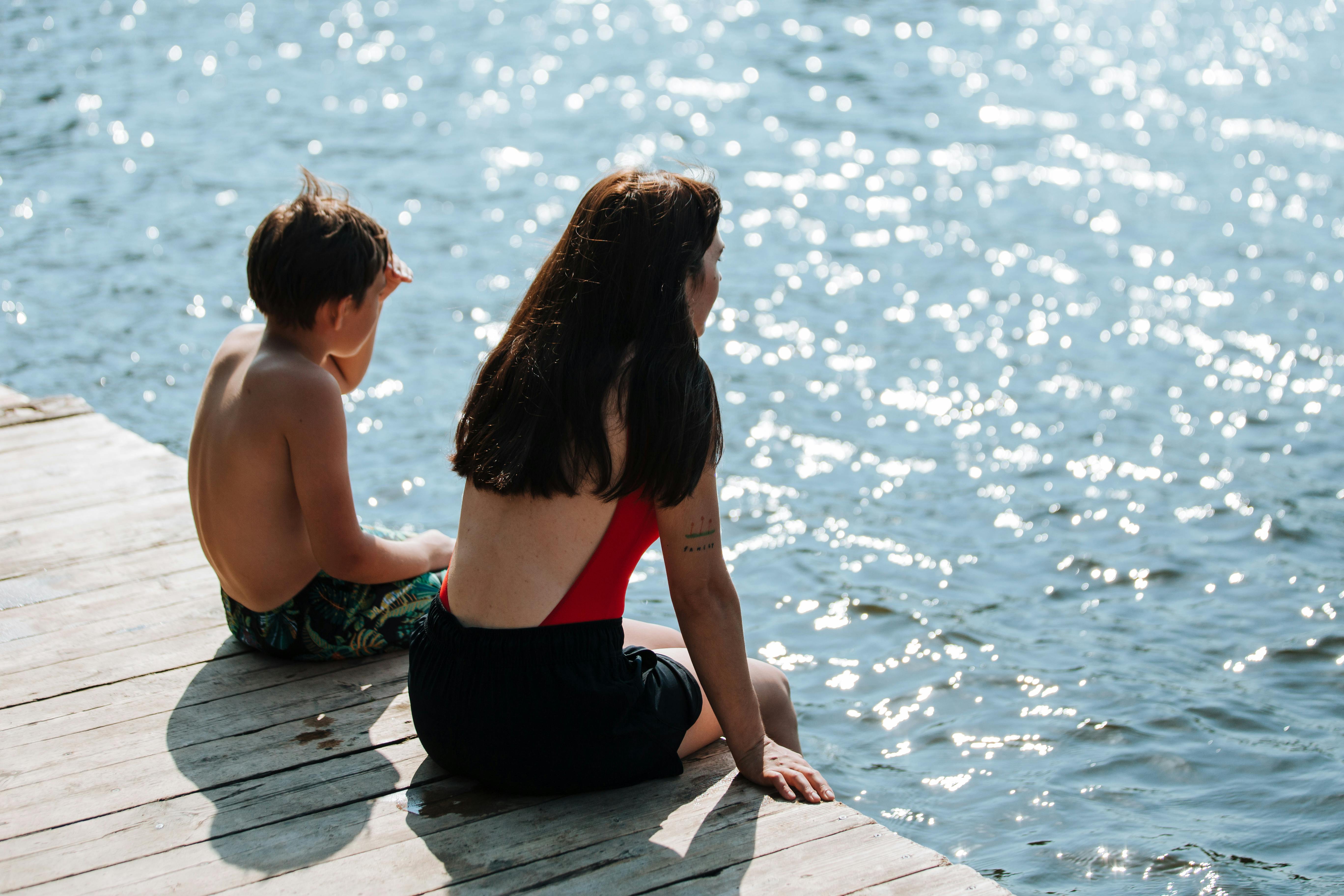 son and mother sitting on lake pier