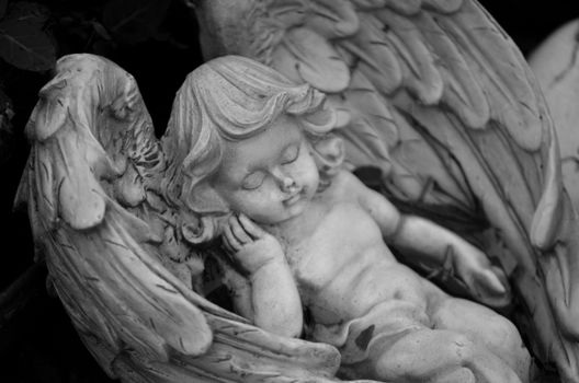Close-up of a detailed carved stone angel figurine with wings, captured in grayscale.