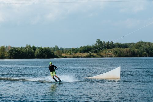 Free Dynamic wakeboarding scene on a sunny lake with lush greenery in the background. Stock Photo