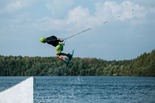 Free Man performing a high-flying wakeboarding stunt on a lake against a forest backdrop. Stock Photo