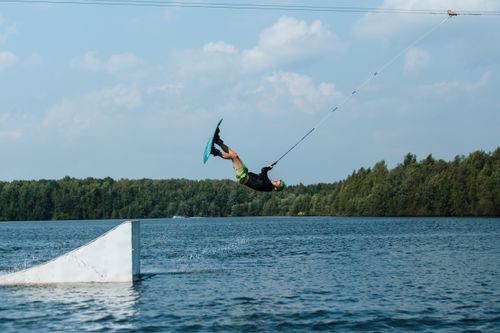 Free A man performs an impressive wakeboarding stunt, mid-air over a ramp on a sunny lake. Stock Photo