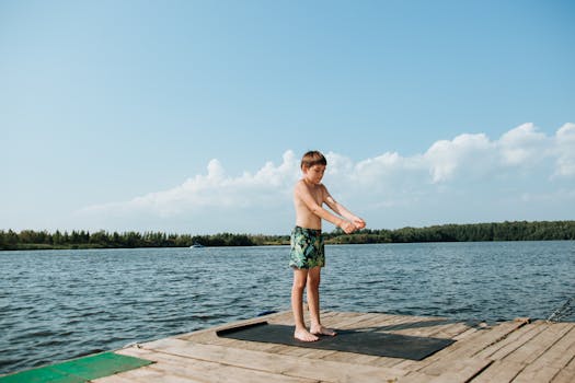 A child enjoying an active lifestyle, stretching on a lakeside dock during summer.