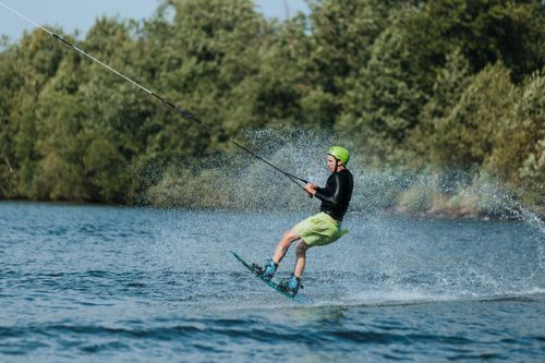 Free A man wakeboarding on a beautiful sunny day, creating splashes while gliding across a lake. Stock Photo