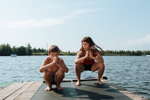 A mother and son exercising on a dock by a serene lake on a sunny day.