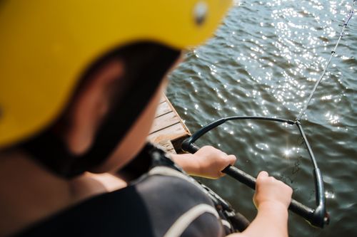 Free Close-up of child holding a wakeboard handle on a sunny lakeshore, ready for action. Stock Photo