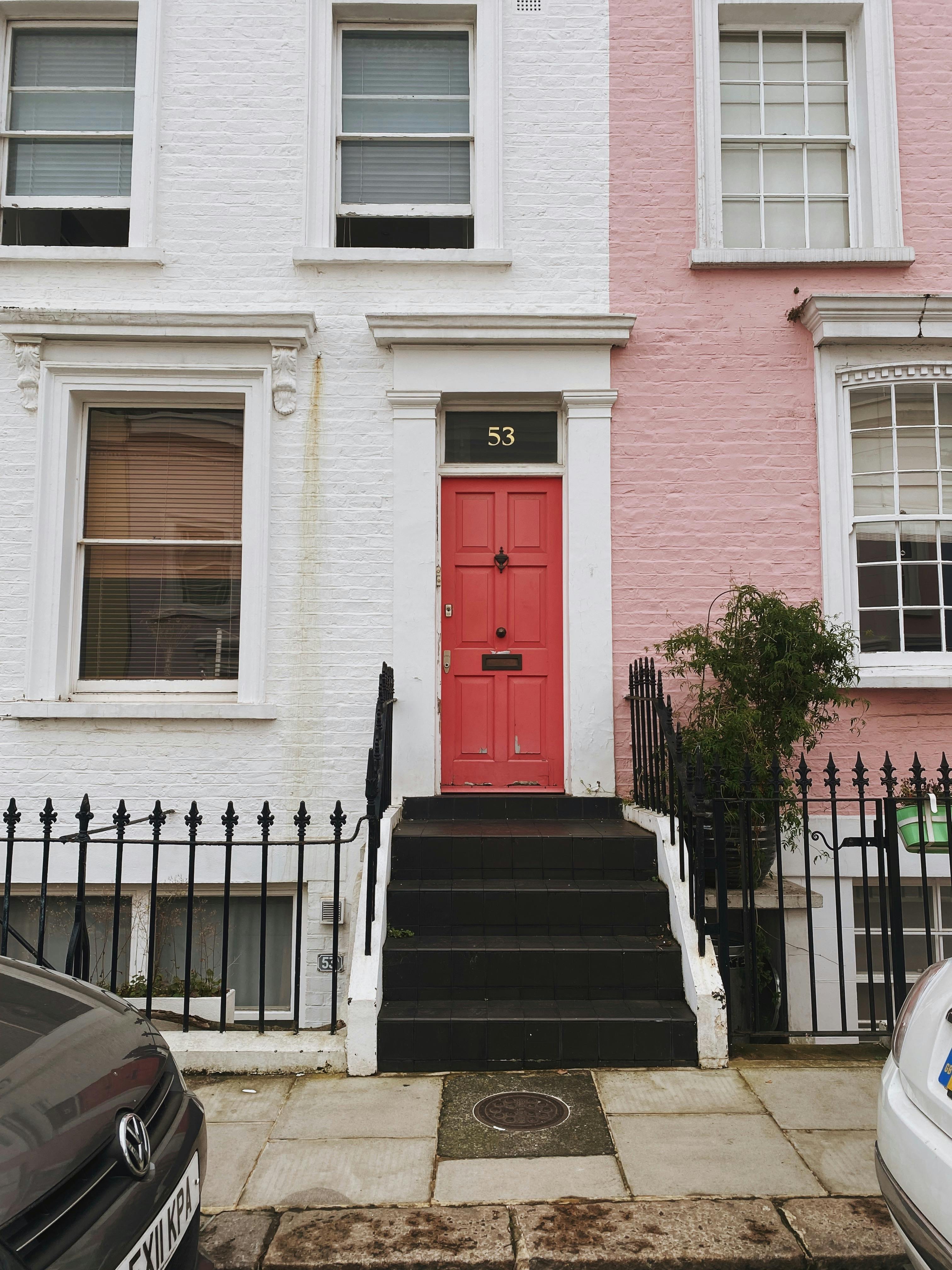 Elegant pink and white facade featuring a classic red door and black railings.
