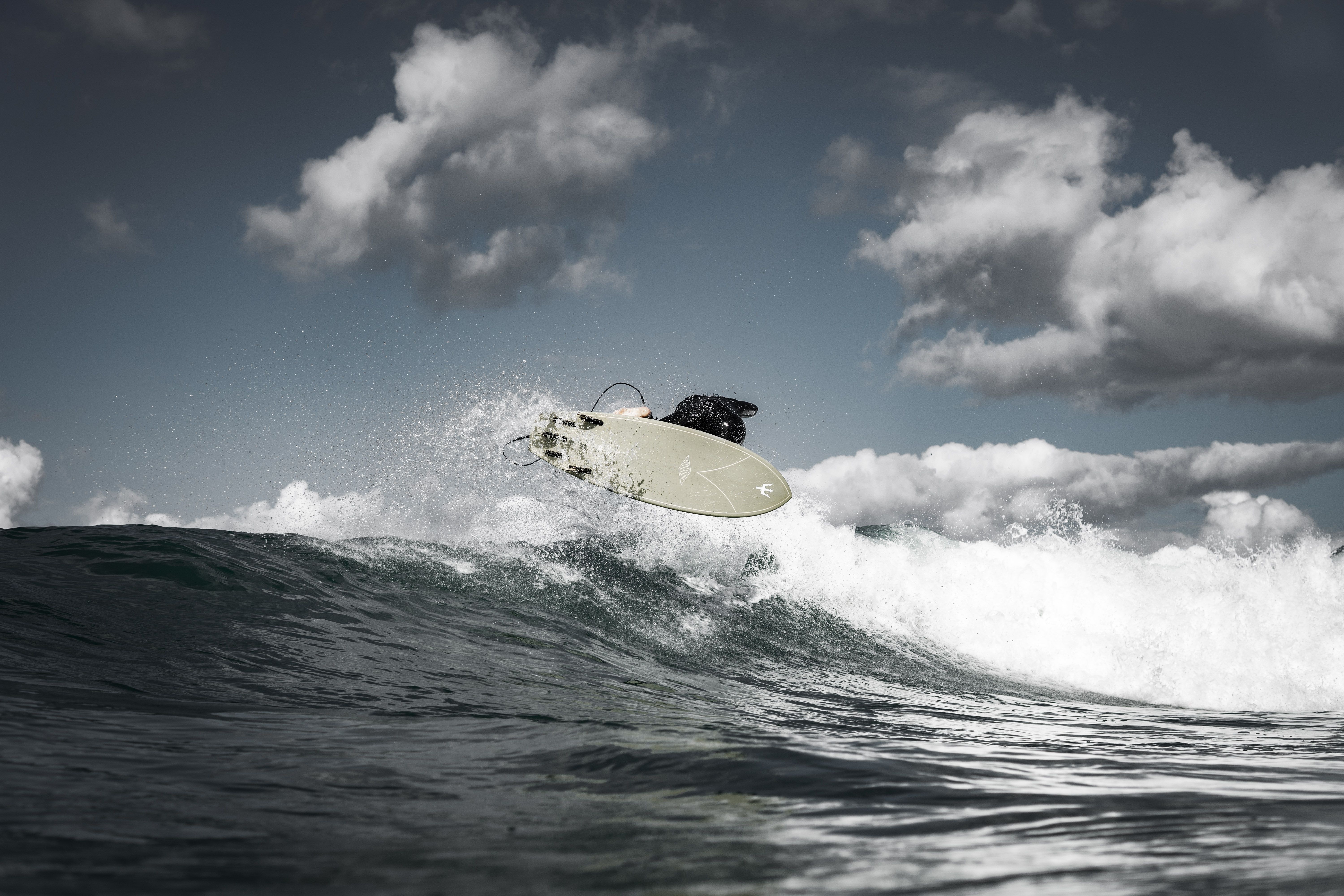 Intense moment of a surfer catching air over the waves against a cloudy sky.