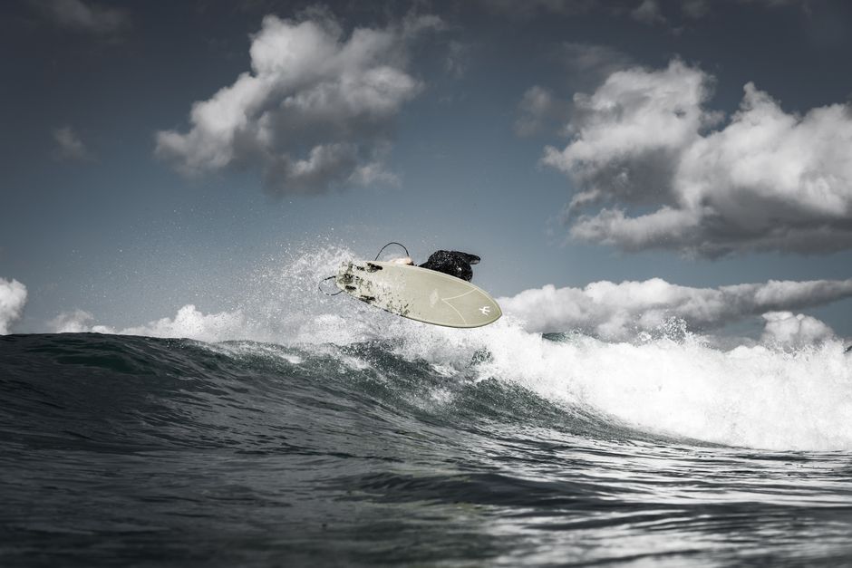 Intense moment of a surfer catching air over the waves against a cloudy sky.
