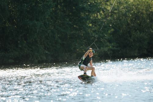 Free A young boy skillfully wakeboarding on a sunny lake day. Stock Photo