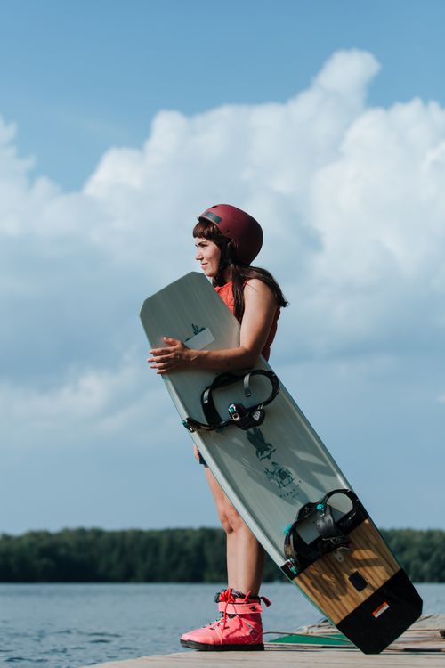 Free Woman standing on a pier with wakeboard and helmet, ready for wakeboarding adventure. Stock Photo