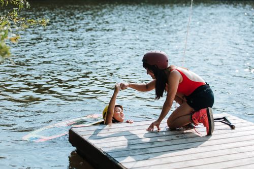 Free A woman assists a boy with a life vest on a pier during a sunny adventure by the lake. Stock Photo