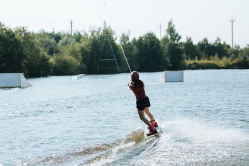 Free A woman with long hair wakeboarding across a scenic lake on a sunny day. Perfect for adventure themes. Stock Photo