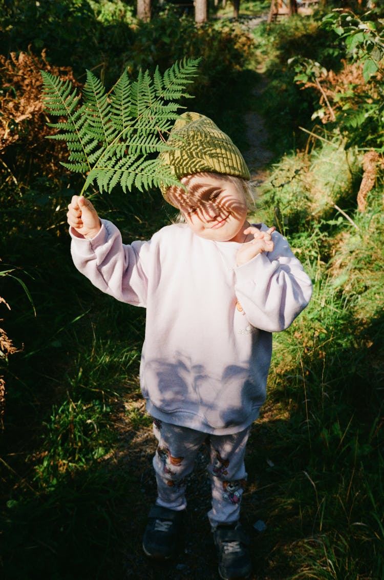 Child Standing In Forest Holding Leaf