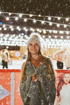 Smiling teenage girl in winter attire enjoying a snowy evening at an outdoor ice rink with festive lights.