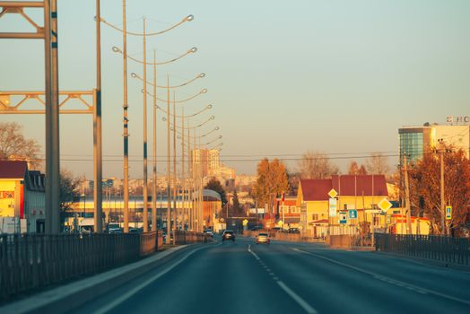 A serene urban street scene at sunset, capturing vehicles and city buildings with a warm glow.