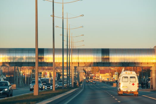 A busy urban highway scene with an ambulance and cars at sunset, showcasing modern architecture.