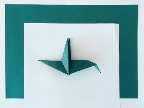 Free A close-up of a teal origami bird on contrasting white and teal paper background. Stock Photo