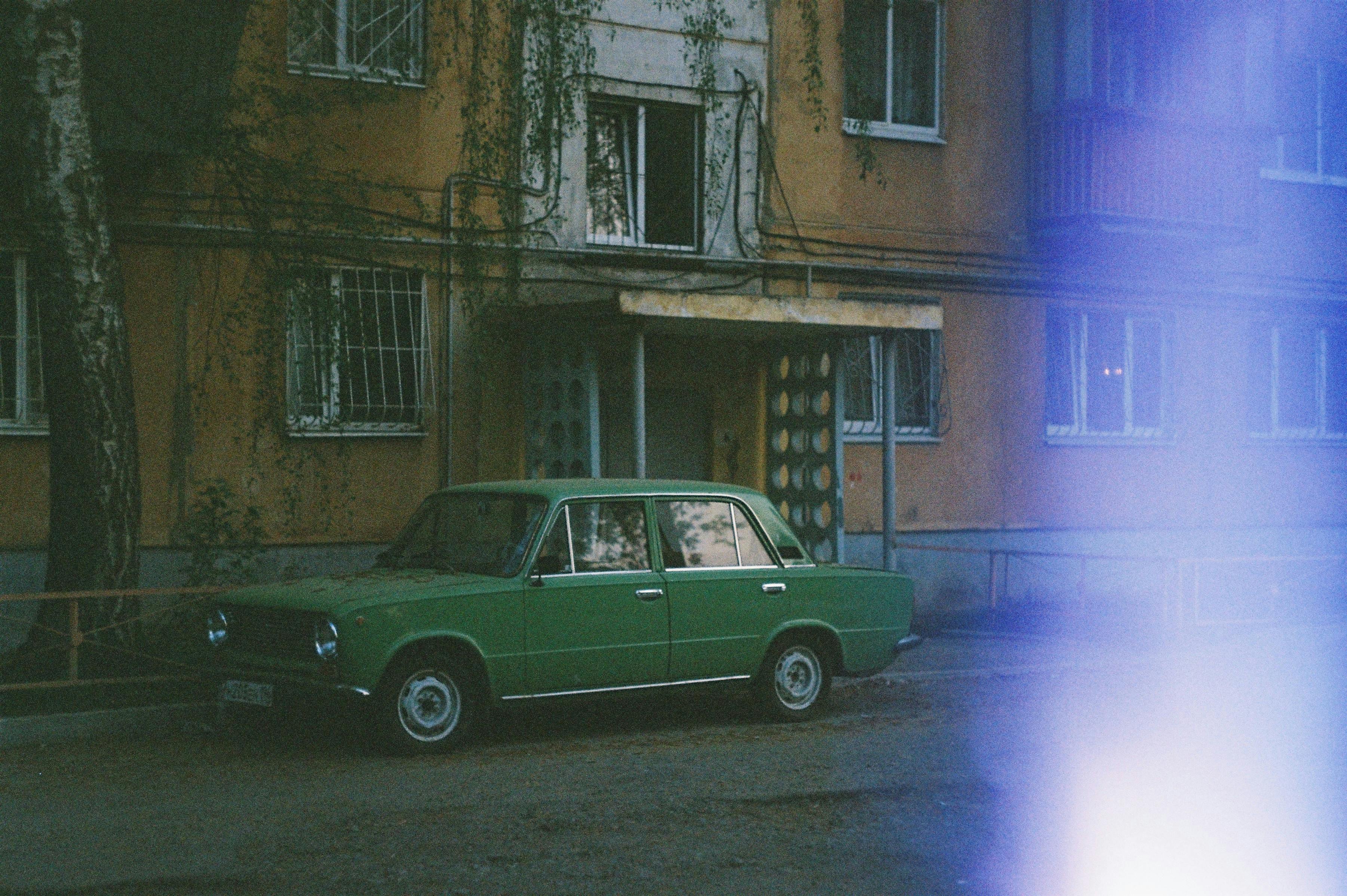 A classic green car parked outside an old building on a street, exuding a vintage vibe.