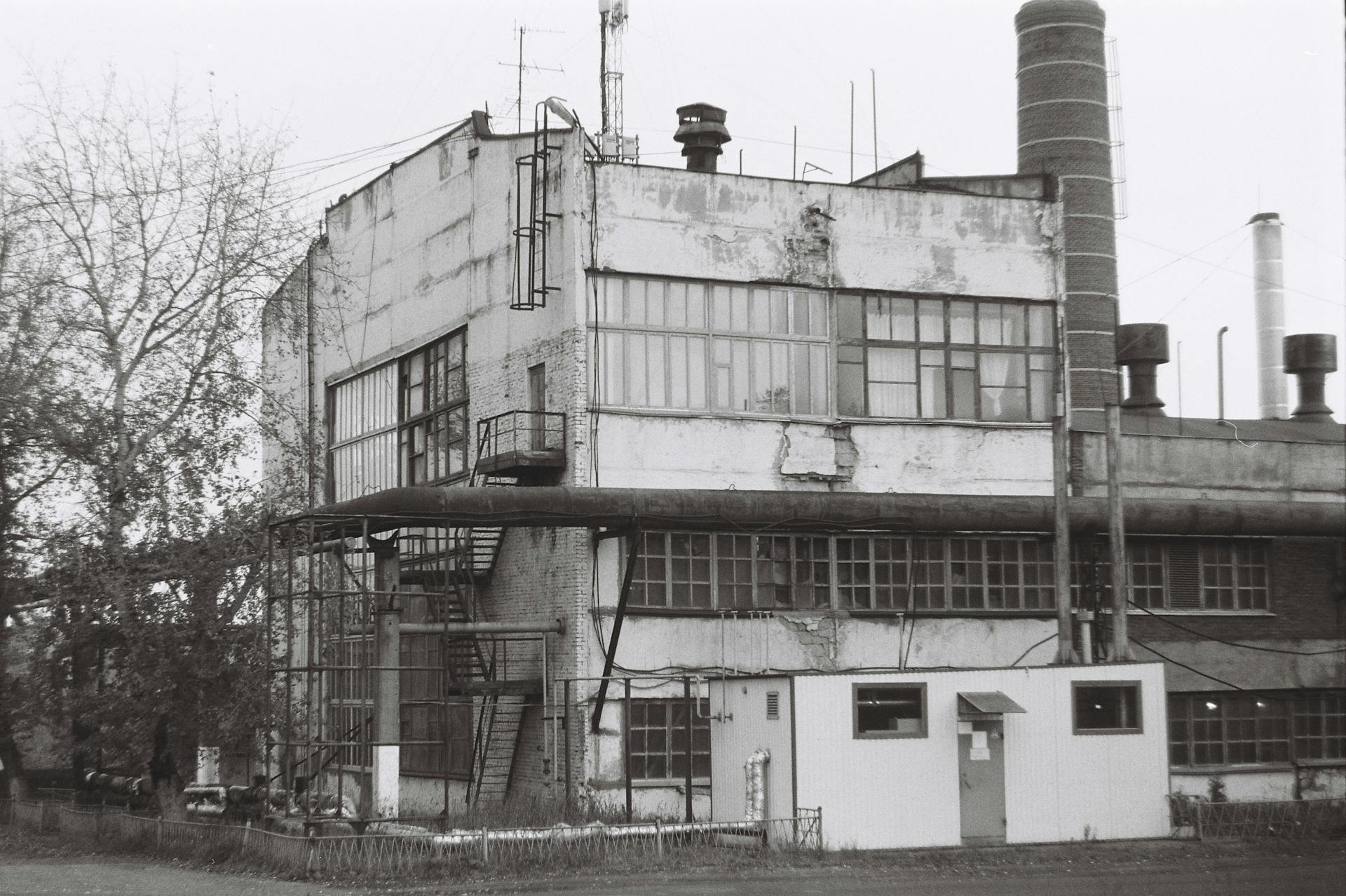 A monochrome image of an old, abandoned industrial building with visible decay.