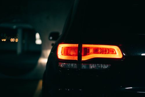 Free A sleek vehicle's tail light glowing vividly in a dimly lit urban setting. Stock Photo