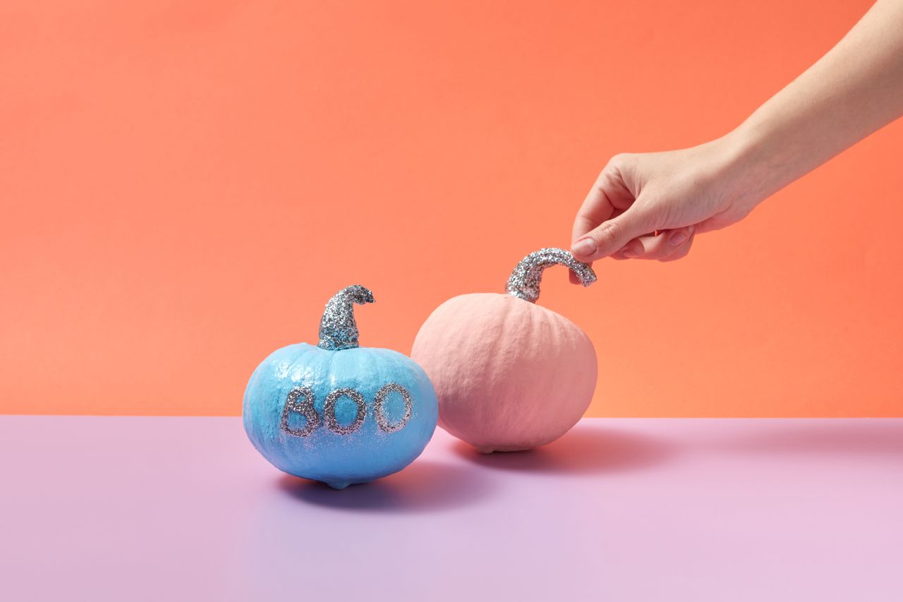 hand holding pink pumpkin with glitter stem next to blue pumpkin with