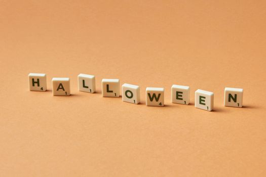 Scrabble tiles spelling 'Halloween' on a flat orange surface, suitable for festive themes.