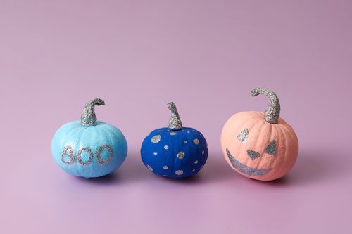 Free Three creatively painted pumpkins with glitter details on a light purple background. Stock Photo