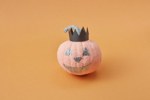 Free A cute mini pumpkin with glittery Jack-o'-lantern face and paper crown on orange background. Stock Photo