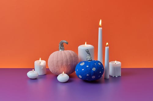 Lighted White Candles near Colored Pumpkins 