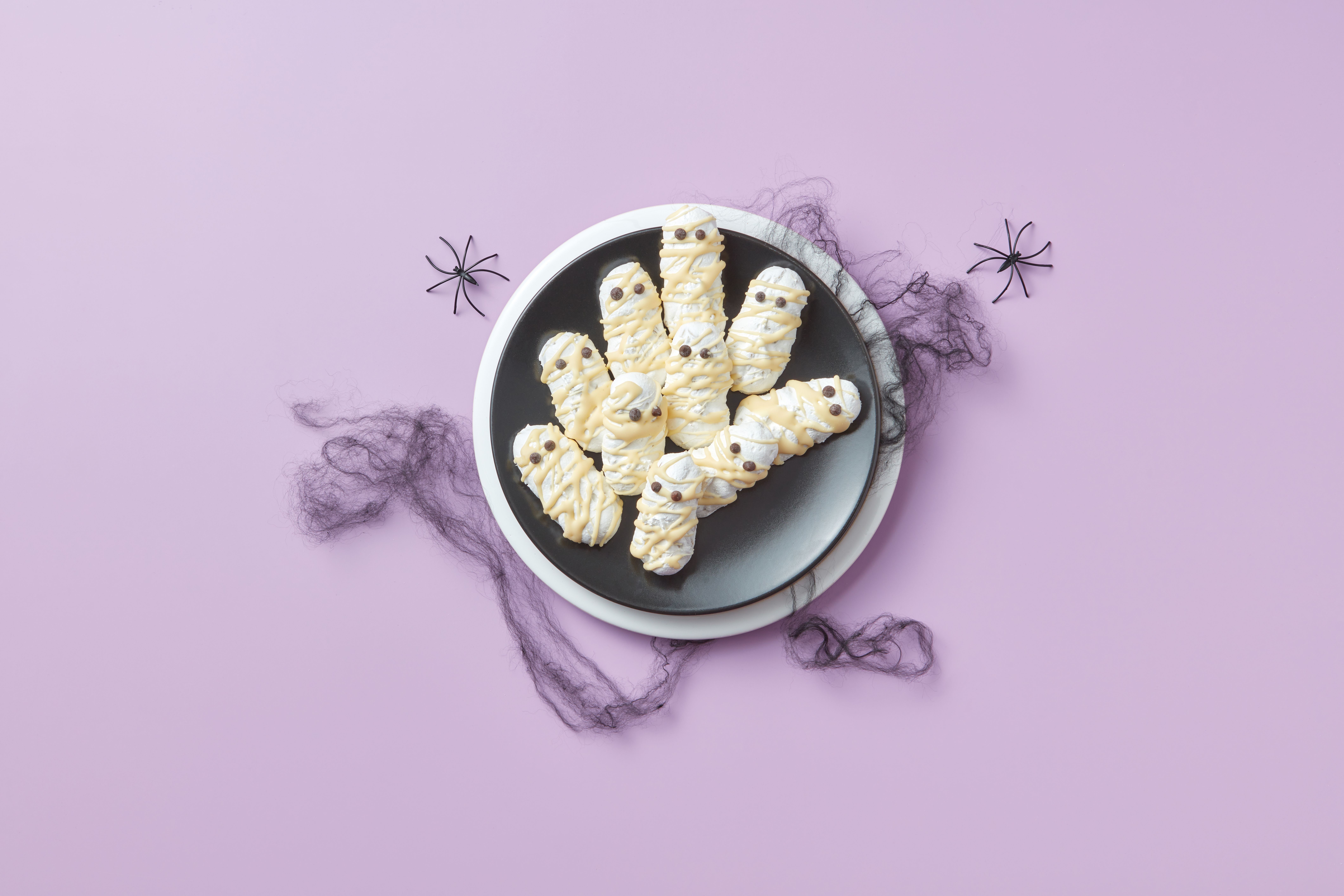 Creative Halloween themed cookies shaped like mummies on a purple background with decorative spiders.