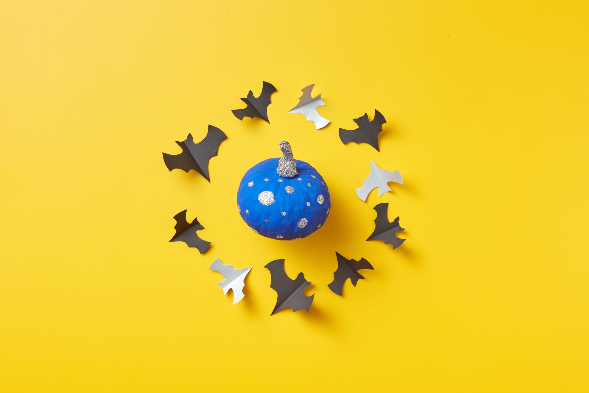 Festive Halloween decor featuring a blue pumpkin surrounded by bat cutouts on a bright yellow background.